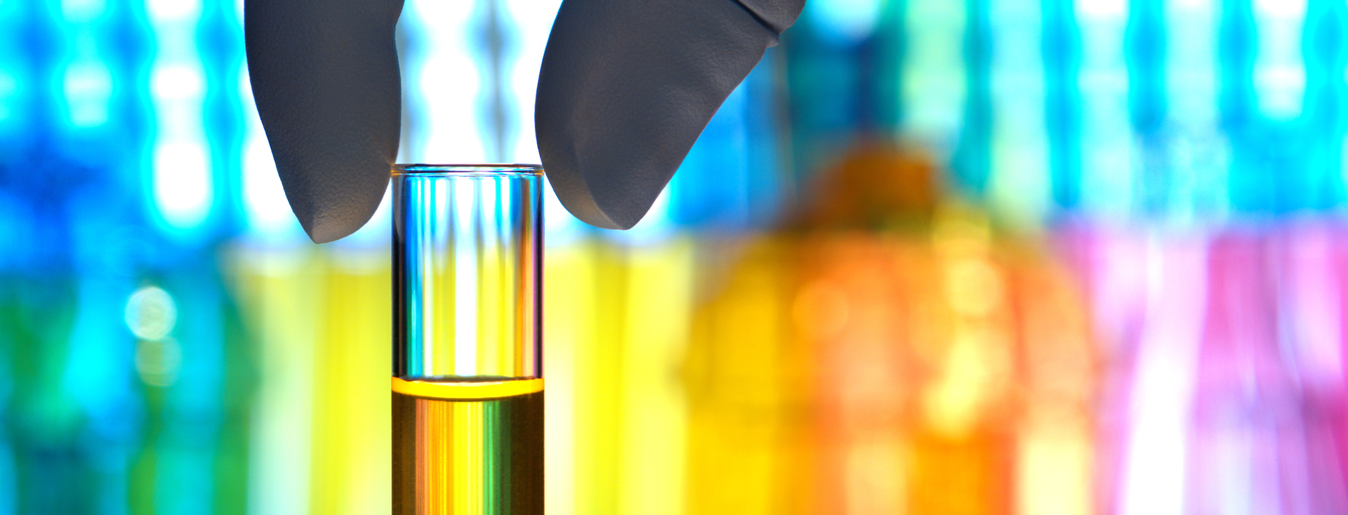 sample vessel with yellow liquid in front of a colourful laboratory background